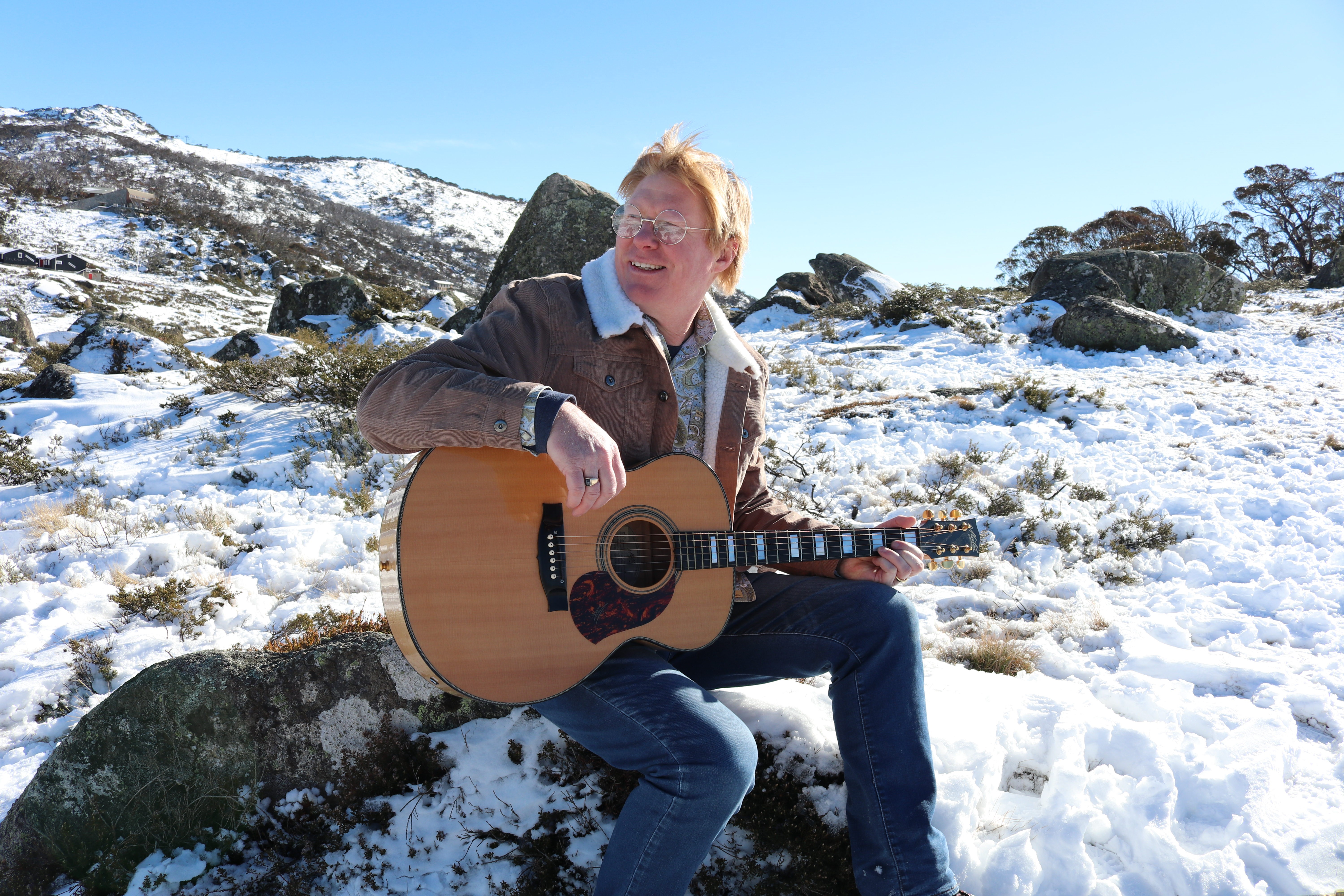 Photo of Darren Coggan as John Denver sitting in snow